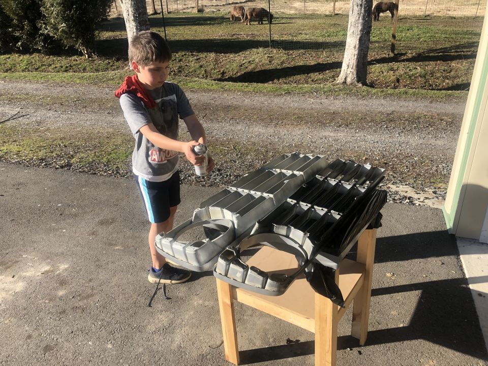 Two grilles on a table, one silver and one black, with a boy spraying one with a can
