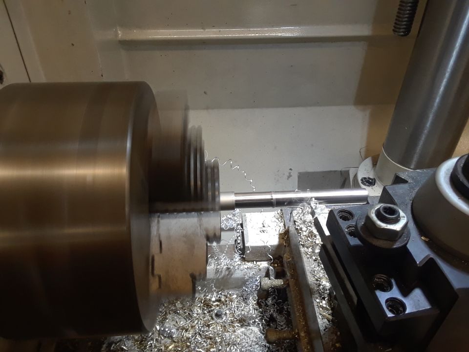 Metal rod with threads being cut on a lathe, with metal shavings scattered around
