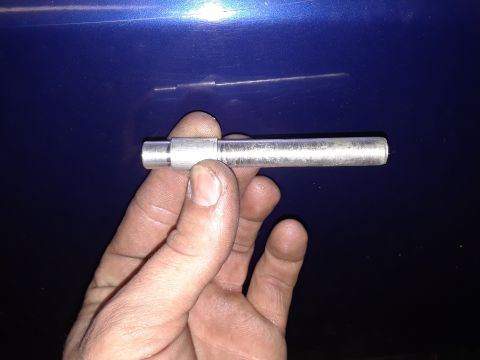 1985 Ford Bronco - A metal rod part is held in a hand against a blue surface.