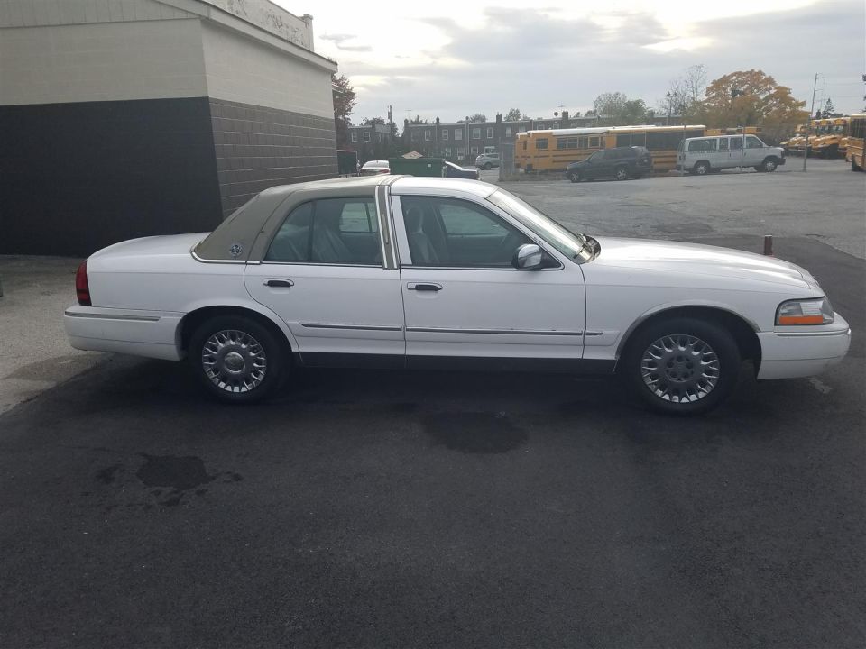 White sedan with tan vinyl half-roof, side profile view, parked near school buses