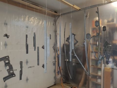 1978 Ford Bronco - Various car parts, possibly door frames and trim pieces, are suspended and ready for painting in a spray booth.