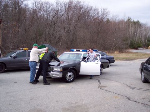 2001 Ford Crown Victoria - Three men are involved in an interaction near a police car, with two other vehicles visible in the background.