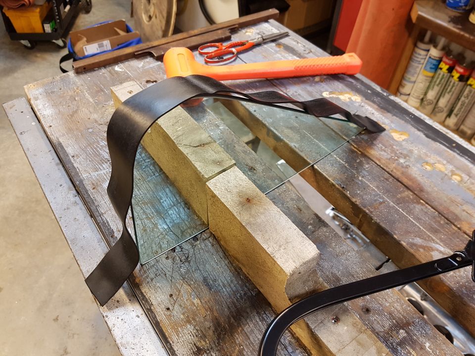 Glass panel and black seatbelt on wooden workbench with tools