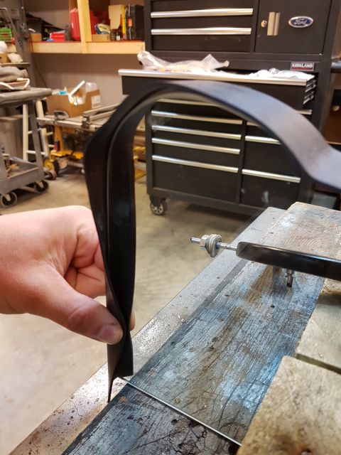 1978 Ford Bronco - A hand holds a black rubber seal, possibly for a vehicle part, in a workshop setting.