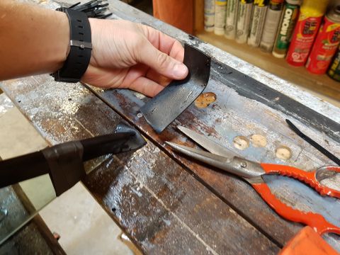 1978 Ford Bronco - A hand holds a bent metal piece over a workbench, with a pair of scissors nearby. The image is from a build thread.
