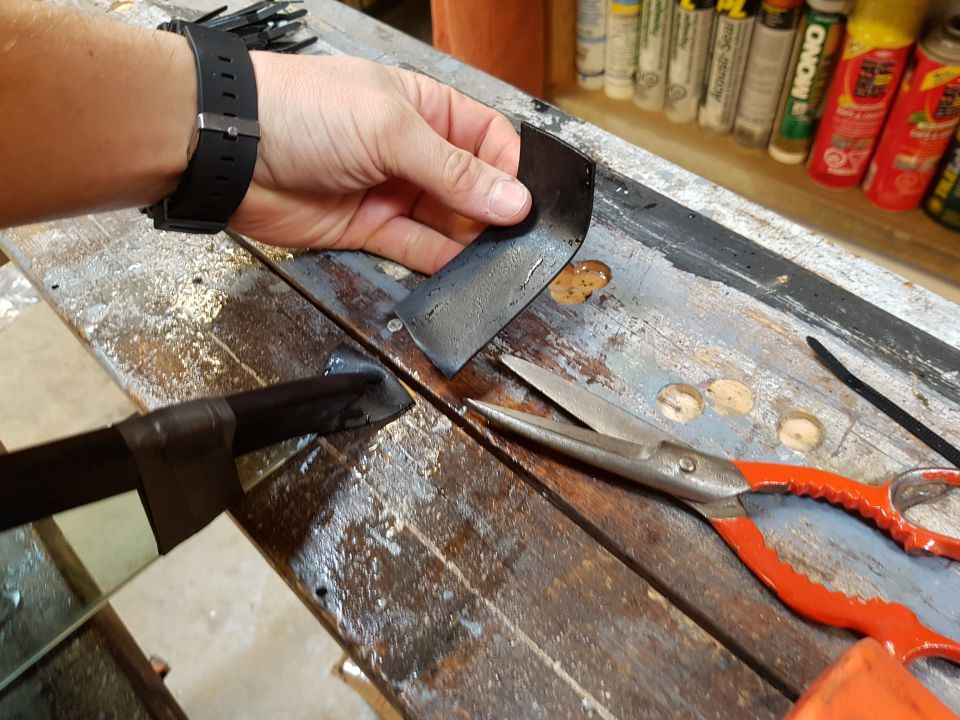 Hand holding a bent metal piece over a workbench with scissors