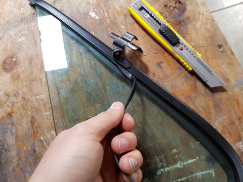 1978 Ford Bronco - Close-up of a hand working on car window trim with a utility knife nearby.