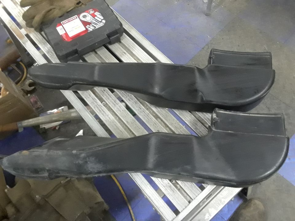 Two black plastic air intake ducts resting on a metal rack next to a toolbox and gloves