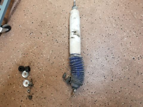 1993 Ford Bronco - A single shock absorber lies on a speckled floor next to a few bolts and washers.