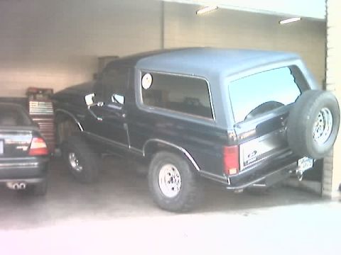 1985 Ford Bronco - A dark-colored Ford Bronco is parked indoors, showing its rear and side profile.