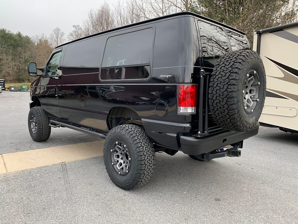Black van lifted with large off-road tires and a spare tire mounted on the back