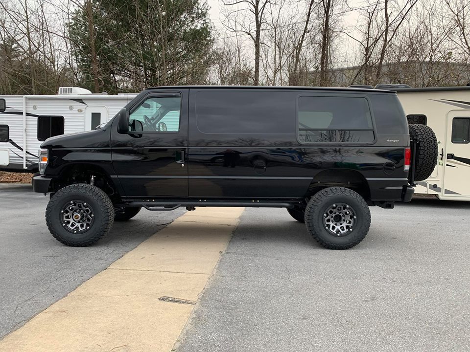 Black van with lifted suspension and off-road tires, parked next to a trailer