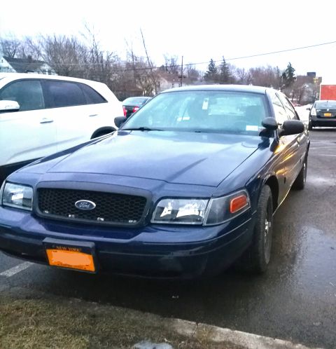 2009 Ford Crown Victoria - A blue 2009 Ford Crown Victoria is parked outside, with another vehicle visible to the left and a dark car in the background.