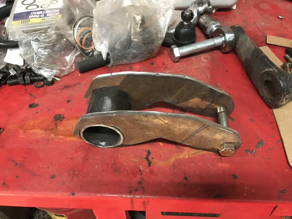 Custom suspension parts with rubber bushings and bolts on a red workbench. A box of assorted O-rings is in the background
