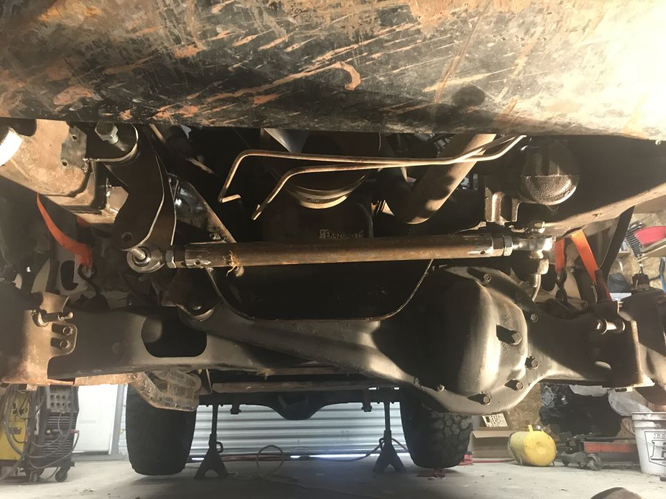 Underside view of a vehicle's drivetrain and suspension components, with the vehicle raised on jack stands