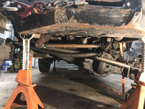 1984 Ford Bronco - Underbody view of a vehicle's suspension and drivetrain components, raised on jack stands for maintenance.