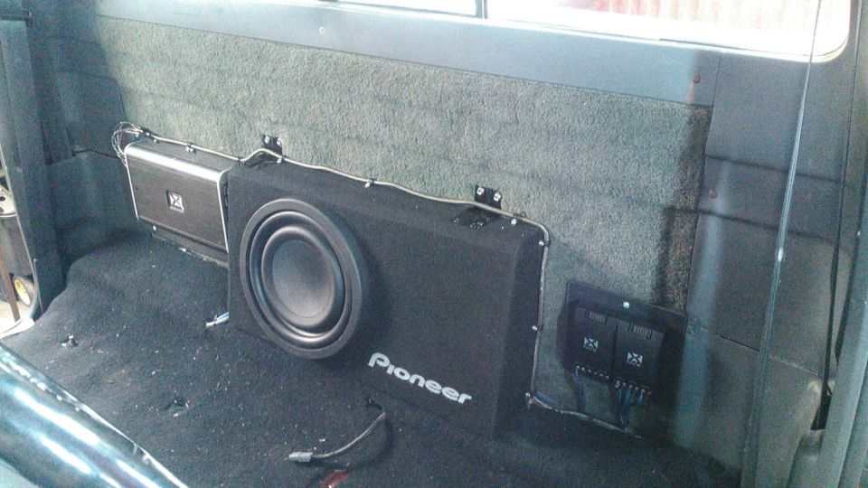 Interior shot of a vehicle's rear seat area showing a Pioneer subwoofer and an amplifier mounted on the back wall