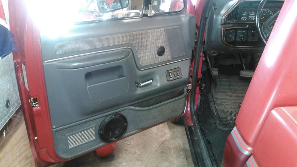 Red truck interior, driver's side door panel with gray fabric insert, speaker, and power window controls. Dashboard visible