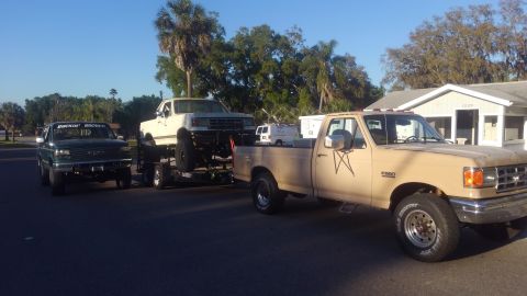 1988 Ford Bronco - Three Ford trucks are visible, including a tan F-250 towing a white Bronco and a green Bronco in the foreground.