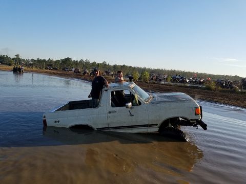 1988 Ford Bronco - A white pickup truck is stuck in a muddy area with several other vehicles in the background.