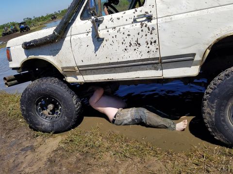 1988 Ford Bronco - Person working on a muddy 1988 Ford Bronco at a mud park with other vehicles in the background.