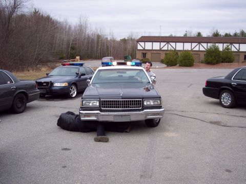 2001 Ford Crown Victoria - A person works on the underside of a police car while two other police cars are nearby.