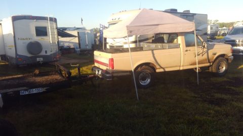 1990 Ford F-250 - A tan Ford pickup truck is parked on grass next to a trailer, with RVs and a canopy in the background.