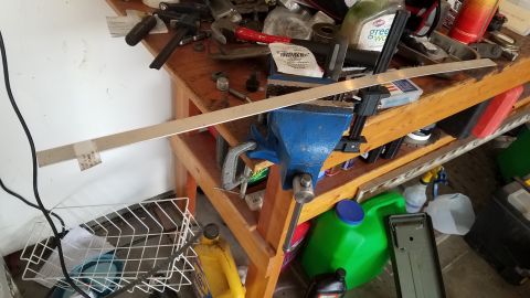 1985 Ford Bronco - A cluttered workbench holds various tools, a metal bar secured in a vise, and several containers.
