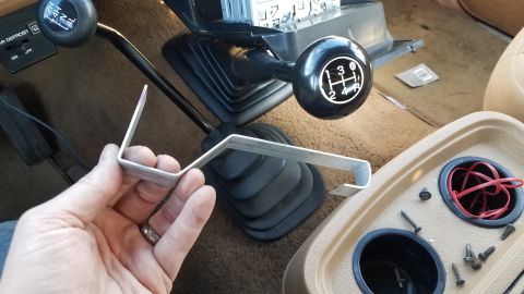 1985 Ford Bronco - Close-up of a metal bracket held near the gear shifter inside a 1985 Ford Bronco.