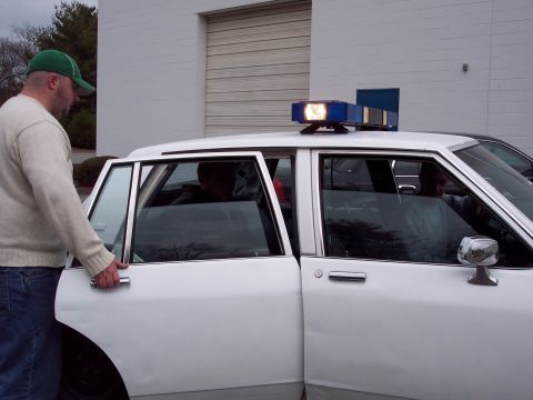 2001 Ford Crown Victoria - A man opens the driver's side door of a white police car parked in front of a building.