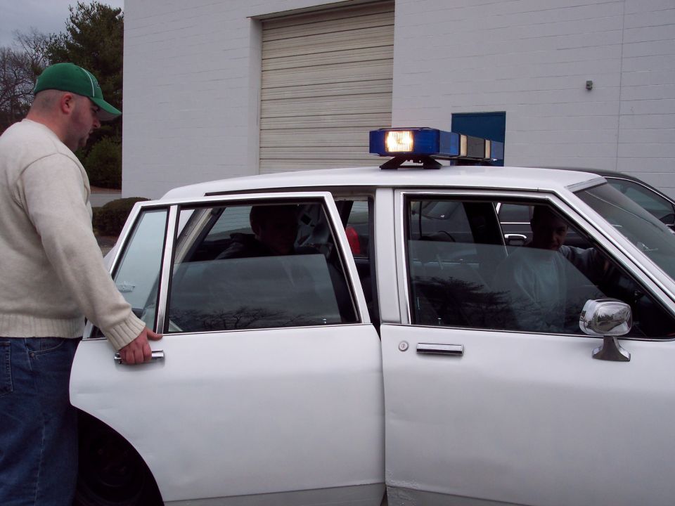 man opening driver door of white police car with light bar on roof