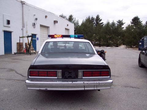 2001 Ford Crown Victoria - Rear view of a police car with a light bar parked in front of a building.