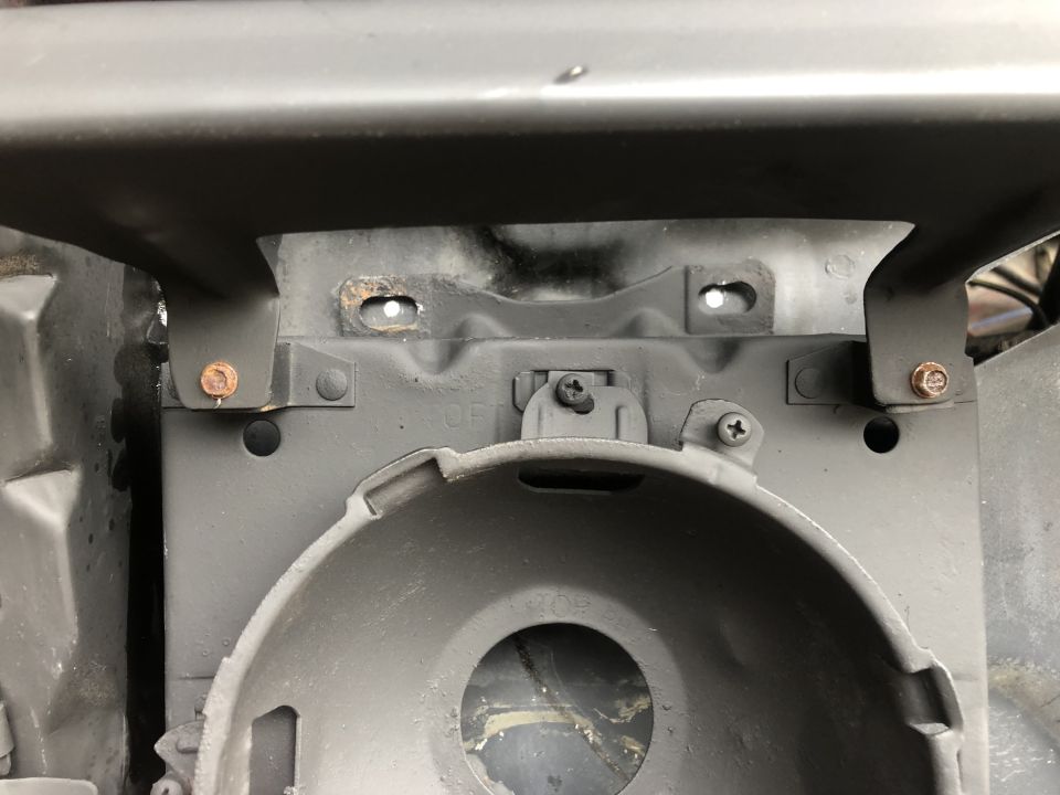 Close-up of a vehicle's headlight mounting bracket with visible rust and screws