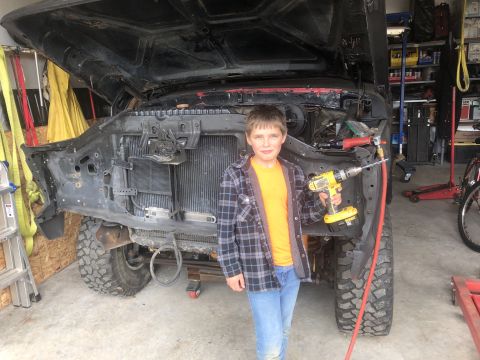 1978 Ford Bronco - A young boy stands in front of a disassembled truck, holding a drill, with the hood open.