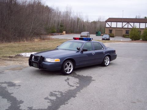 2001 Ford Crown Victoria - A blue 2001 Ford Crown Victoria police car is parked in a lot with a push bumper and light bar.