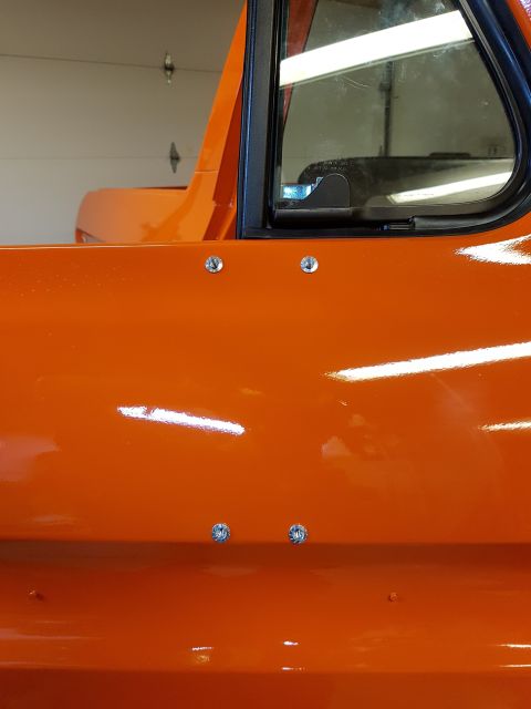 1978 Ford Bronco - Close-up of an orange vehicle's side panel, showing rivets and a website watermark.