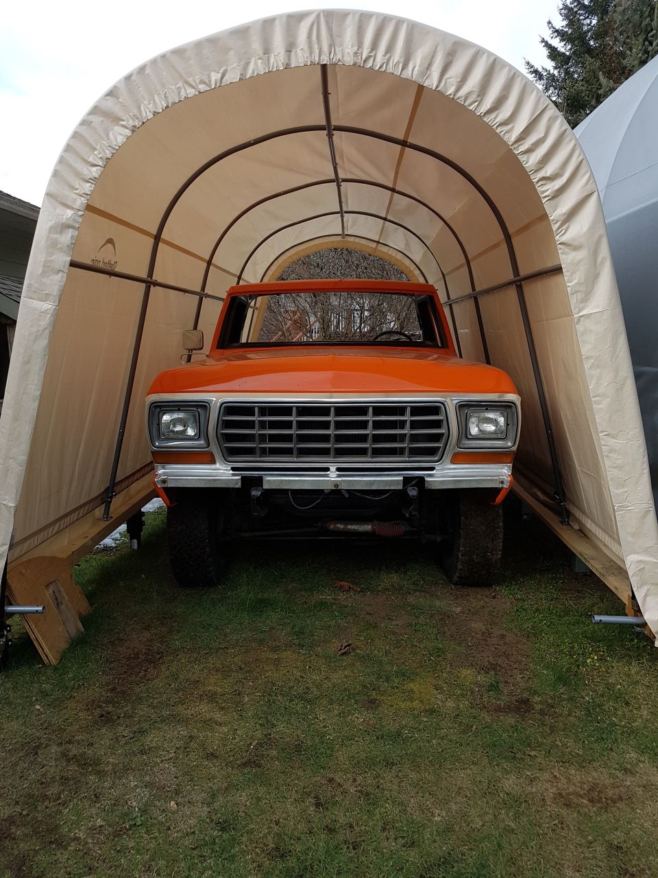 Orange pickup truck parked inside a portable garage. Front view shows grille and headlights