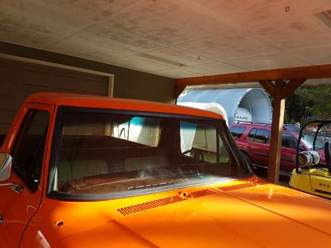 1978 Ford Bronco - The front of an orange truck is visible, with a red SUV parked behind it under a covered structure.