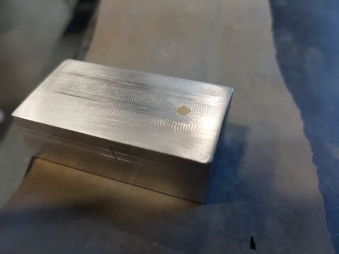 1978 Ford Bronco - A close-up view of a machined metal block, possibly a vehicle part, with a brushed texture and a small brass insert.