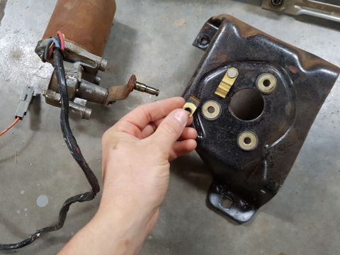 1978 Ford Bronco - A person is holding a small metal component next to a disassembled windshield wiper motor and bracket assembly.