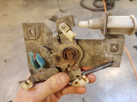 1978 Ford Bronco - Close-up of a rusty door latch mechanism, showing its internal components and a white actuator. The part is held by a hand.