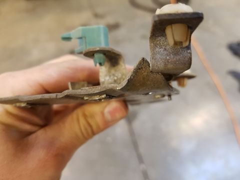 1978 Ford Bronco - Close-up of a metal bracket with plastic connectors, held by a hand.