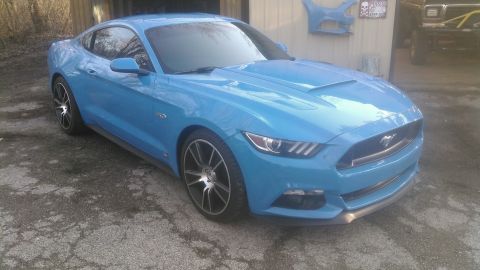2017 Ford Mustang - A bright blue Ford Mustang is parked in front of a garage with some car parts hanging on the wall.