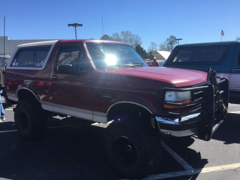 1979 Ford Bronco - Maroon Ford Bronco with a white top and a brush guard, lifted on large tires, parked next to another SUV.