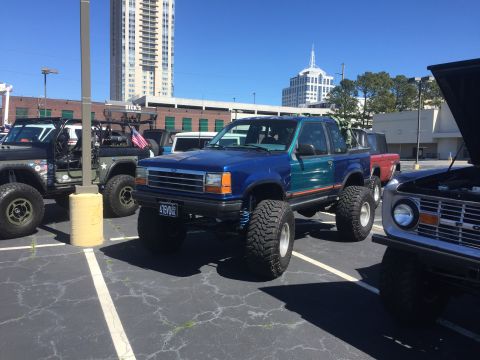 1979 Ford Bronco - Modified Ford pickup truck with custom paint and suspension, parked with other off-road vehicles.