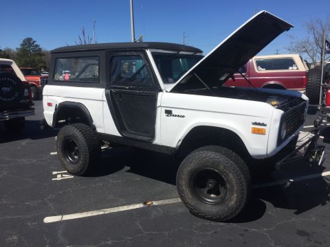 1979 Ford Bronco - A white Ford Bronco is parked in a lot with its hood open, showing off its engine bay.