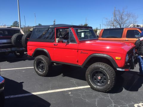 1979 Ford Bronco - A red 1979 Ford Bronco is parked in a lot next to another vehicle.