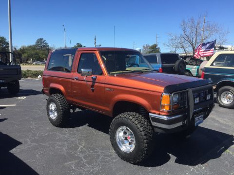 1979 Ford Bronco - Orange Ford Bronco II, likely a late 1980s model, parked outdoors.
