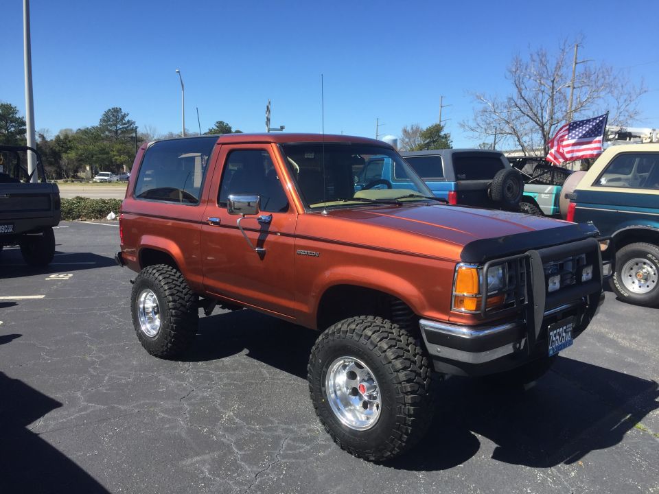 Orange Ford Bronco II with aftermarket wheels and tires, parked in a lot with other vehicles
