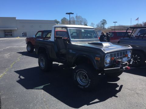 1979 Ford Bronco - A dark green Ford Bronco with a white top is parked in a lot next to other vehicles.